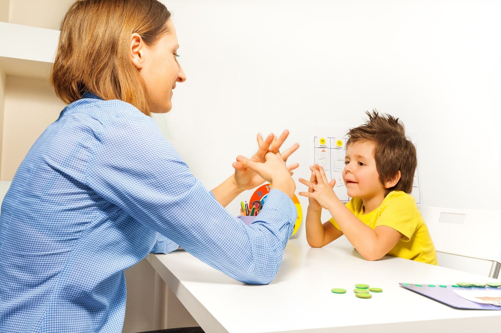 An ABA therapist and a young child doing a hand-clapping motor imitation exercise together